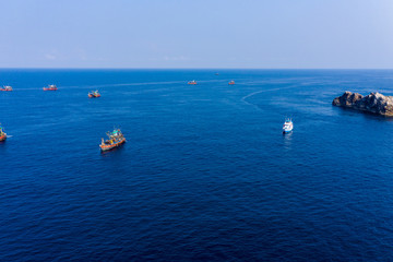 Overfishing - Aerial done view of a fleet of fishing trawlers clustered around a tiny, rocky island (Mergui, Myanmar)