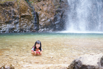 Asian child cute or kid girl and hill tribe happy smiling with fun and enjoy playing water splash on waterfall or river and holiday relax trip for summer travel at Jokkradin waterfall with space