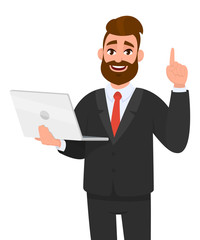 Young business man holding/showing latest brand new laptop computer device and pointing finger up or gesturing/showing number one with hand finger. Modern lifestyle, digital technology trend, gadget.