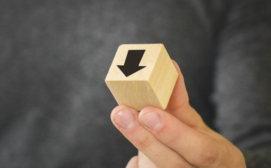 wooden cube in the hand of a man with a black arrow black arrow means fall and degradation,...