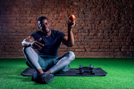 Sportive detox african american man resting after training with apple and smartphone in hand