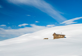 Panoramic view across snow covered slope on alpine mountain with small house
