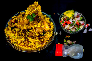 Popular Indian & Asian kashmiri dish i.e. yakhni or akhni in a glass plate along with some salad and salt on black colored shiny surface.