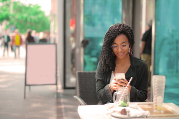 Pretty Afro woman texting on a café's terrace.
