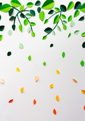 White background with falling green yellow orange leaves and branches of paper, handmade