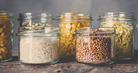 Various raw cereals, grains, beans and pasta for cooking healthy food in glass jars on a wooden...
