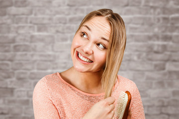 Portrait of a beautiful smiling young woman comb hair, on brick wall background