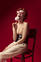 Medieval redhead young woman as a duchess in black corset, sunglasses and night clothes sitting on...