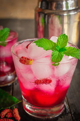 Fresh Ice Mulberry Soda drink on the wood table there are Mulberry, Leaves, cocktail shaker and same object placed around.