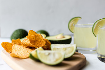 Fresh avocado, lime, drink and nacho chips lying on marble background. Recipe for Cinco de Mayo party