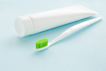 Toothbrush with green bristles and white tube of toothpaste on pastel blue table. Teeth hygiene...