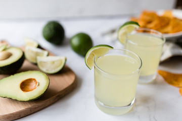 Fresh avocado, lime, drink and nacho chips lying on marble background. Recipe for Cinco de Mayo party