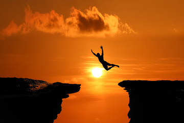 Silhouette of Men are jumped between high cliff at a red sky sunset