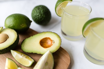 Fresh avocado, lime, drink and nacho chips lying on marble background. Recipe for Cinco de Mayo party