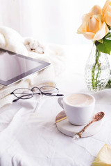 tablet pc computer, coffee cup and beige roses in the morning on the white bed background, flat lay