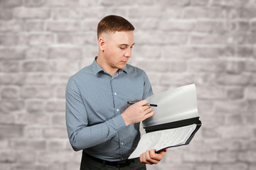 Portrait of handsome young guy holding folder and pen on brick wall background
