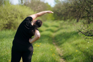 Morning yoga. Young woman doing exercises in summer park, back view. Healthy lifestyle, sport, weight losing, activity concept