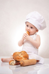 Little baker baby boy with loaf dressed in chef hat, laughing happily
