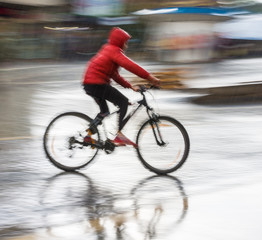 Cyclist on the city roadway in motion blur in rainy day. Intentional motion blur