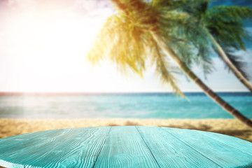 Summer background of wooden table and beach background with palms 