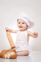 funny cook baby in the cook costume and chef hat with dough rolling pin sitting with bread
