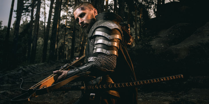 mystery scarface knight in armor with sword and crossbow in the forest