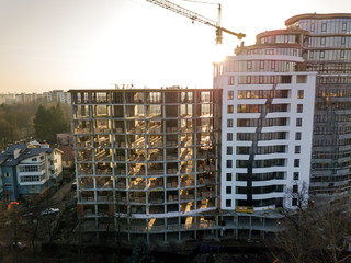 Apartment or office tall building under construction, top view. Tower crane and city landscape stretching to horizon. Drone aerial photography.