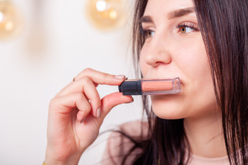 Fototapeta premium Beautiful caucasian girl make up artist, visagiste, model holding pastel beige liquid lipstick, lip gloss. Concept advertising no brand decorative professional cosmetic store