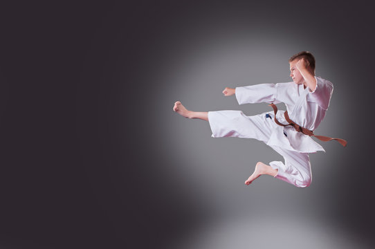 Handsome young male karate player doing kick on the gray background