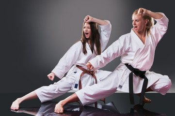 Two beautiful young female karate players doing kata on the gray background