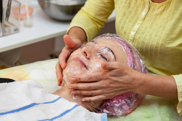 A young girl is lying on a couch during cosmetic procedures with a mask on the faces above which the beautician imposes a transparent film. Cleansing the face.