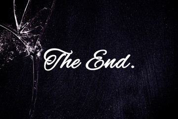 The text The End, written over a worn blackboard surface containing chalk powder, and under a broken glass with sharp shards.