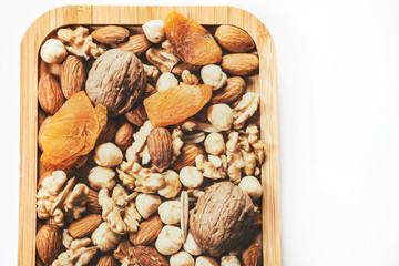 Wooden bowl with mixed nuts on white table top view. Healthy food and snack. Walnut, pistachios, almonds, hazelnuts
