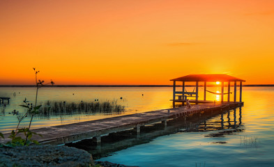 Sunrise over lake bacalar mexico, with dog sitting on the dock