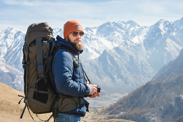 Portrait of a bearded male photographer in sunglasses and a warm jacket with a backpack on his back...