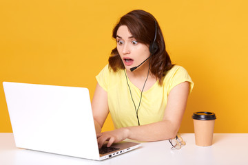 Short haired shocked attractive operator posing with wide opened mouth and eyes, looking at laptop...
