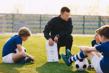 Football coach coaching children. Soccer football training session for children. Young coach teaching kids on football field. Football tactic education. Coach explains the strategy of the game © matimix