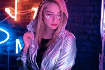 Beautiful young woman wearing metallic bomber jacket trendy stylish glasses stand near brick wall...