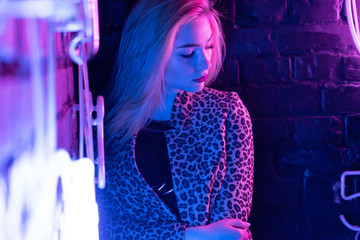 Attractive sexy girl stripper wearing stylish leopard jacket standing near brick wall with purple...