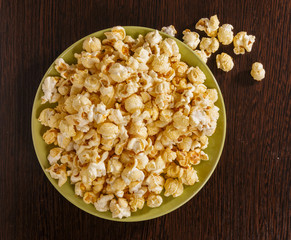 A plate of popcorn is on the table. Pieces of popcorn scattered on the table.