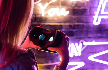 Close up view of girl woman female hands holding vr headset glasses device illuminated with futuristic purple neon lights, wearable virtual augmented reality digital innovation technology concept