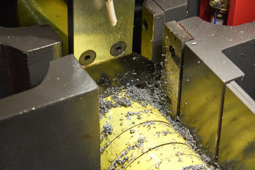 Cutting a round metal bar with a band saw. Chips and drops of oil fly out of the cutting area