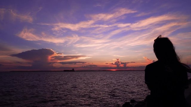 Woman sitting looking at sunset sky at sea beach . Woman silhouette backside view watches evening ocean waves enjoying wind at her face thinking dreaming