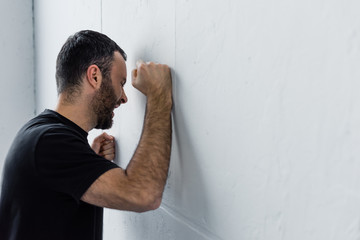 adult depressed man screaming while standing by white wall at home