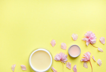 Hand cream, lip balm on a yellow background, flower petals. Space for a text. Copy space. spa flat lay. The concept of beauty and personal care. Natural handmad