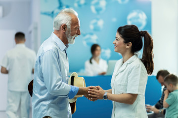 Young doctor and senior patient shaking hands in hallway of the hospital.