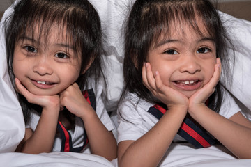 happy little girls twins sister in bed under the blanket having fun, smiling and wacky