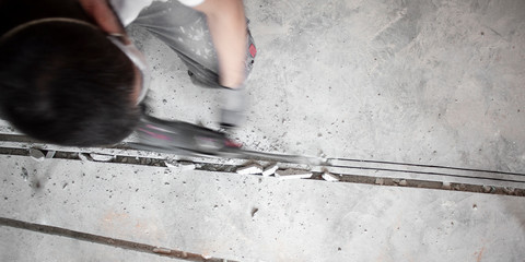 Handwerker stemmt Schlitze in den Estrich auf der Baustelle