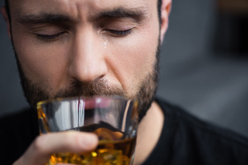 selective focus of depressed bearded man holding glass of whiskey with closed eyes