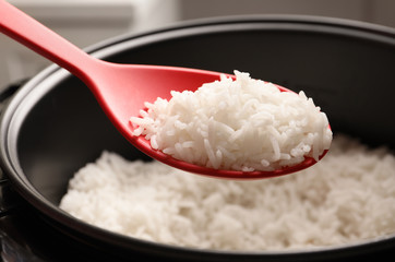 Spoon with tasty hot rice over cooker, closeup